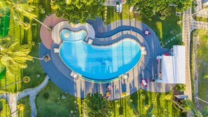 Vista aérea de una piscina de forma peculiar rodeada por una zona ajardinada con senderos y mobiliario.