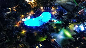A large, illuminated swimming pool with a unique shape, surrounded by palm trees and outdoor lighting. - Ocean Blue Ngwe Saung Beach Hotel (Ngwe Saung)