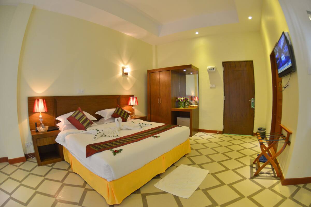 A hotel room with a large bed, two bedside lamps, a wooden wardrobe, a television, and a patterned floor.