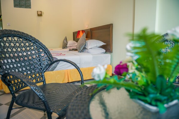 A hotel room with a bed, a wicker chair, and a potted plant.