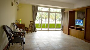 A living room with a TV, a dining table, chairs, and a large window with a view of palm trees. - Ocean Blue Ngwe Saung Beach Hotel (Ngwe Saung)