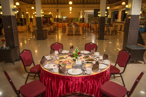 Un comedor con mesas redondas cubiertas con manteles rojos, rodeado de sillas tapizadas en rojo.