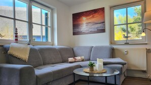 Een moderne woonkamer met een grijze bank, een ronde salontafel met kaarsen, en een schilderij van een zonsondergang.