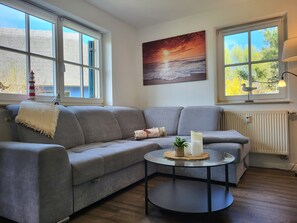 A modern living room with a grey sofa, a round coffee table with candles, and a painting of a sunset.