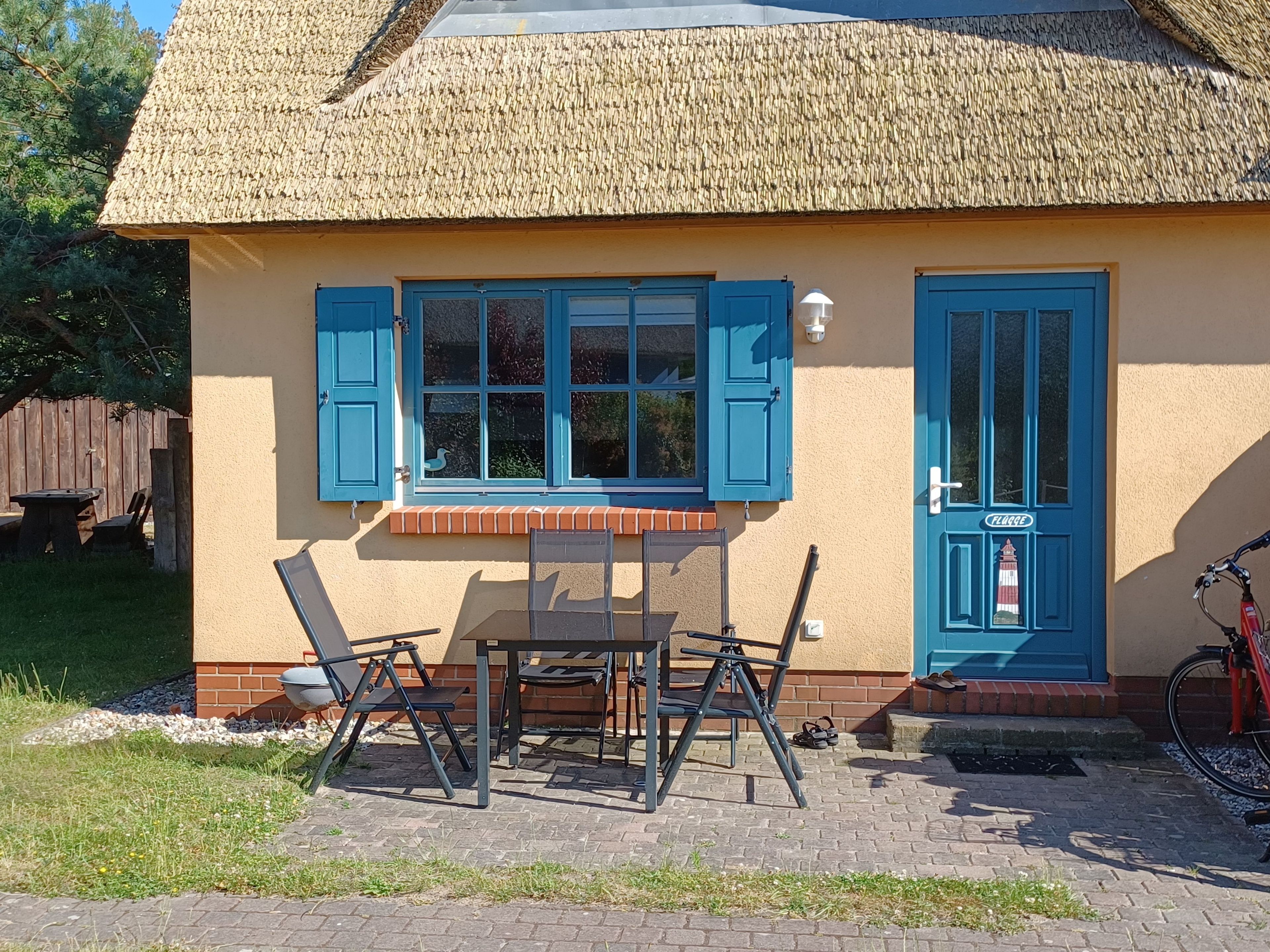 En byggnad med ett halmtak, en blå dörr och ett bord med stolar utomhus.