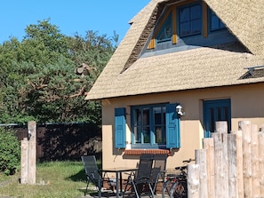 A house with a thatched roof, blue shutters, and a table with chairs outside. - Vacation farm at Fischland Flügge (Wustrow)