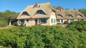Een traditioneel huis met rieten dak, meerdere ramen en een tuin ervoor.