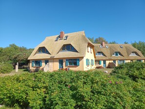 Ein traditionelles Haus mit Strohdach, zahlreichen Fenstern und einem Vorgarten.