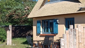Een huis met rieten dak, blauwe luiken en een tafel met stoelen.