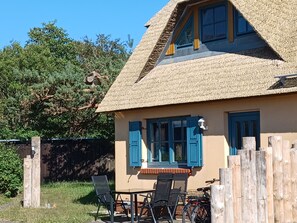 Ein Haus mit Strohdach, blauen Fensterläden und einem Tisch mit Stühlen vor der Tür.