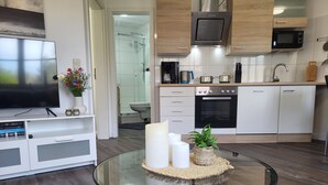 Een moderne keuken met witte kastjes, een magnetron, een oven en een glazen salontafel met kaarsen en een plant.
