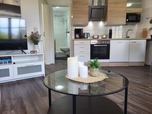 A modern kitchen with white cabinets, a microwave, an oven, and a glass coffee table with candles and a plant.