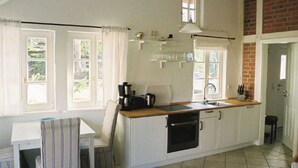A kitchen with white cabinets, a wooden countertop, a sink, and a stove. There is a chair and a table with a striped chair cover.