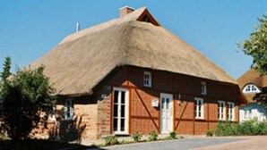 A traditional thatched-roof house with a brick exterior, a central door, and windows on the side.