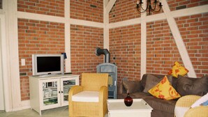 A living room with a brick wall, white furniture, a television, and a fireplace.