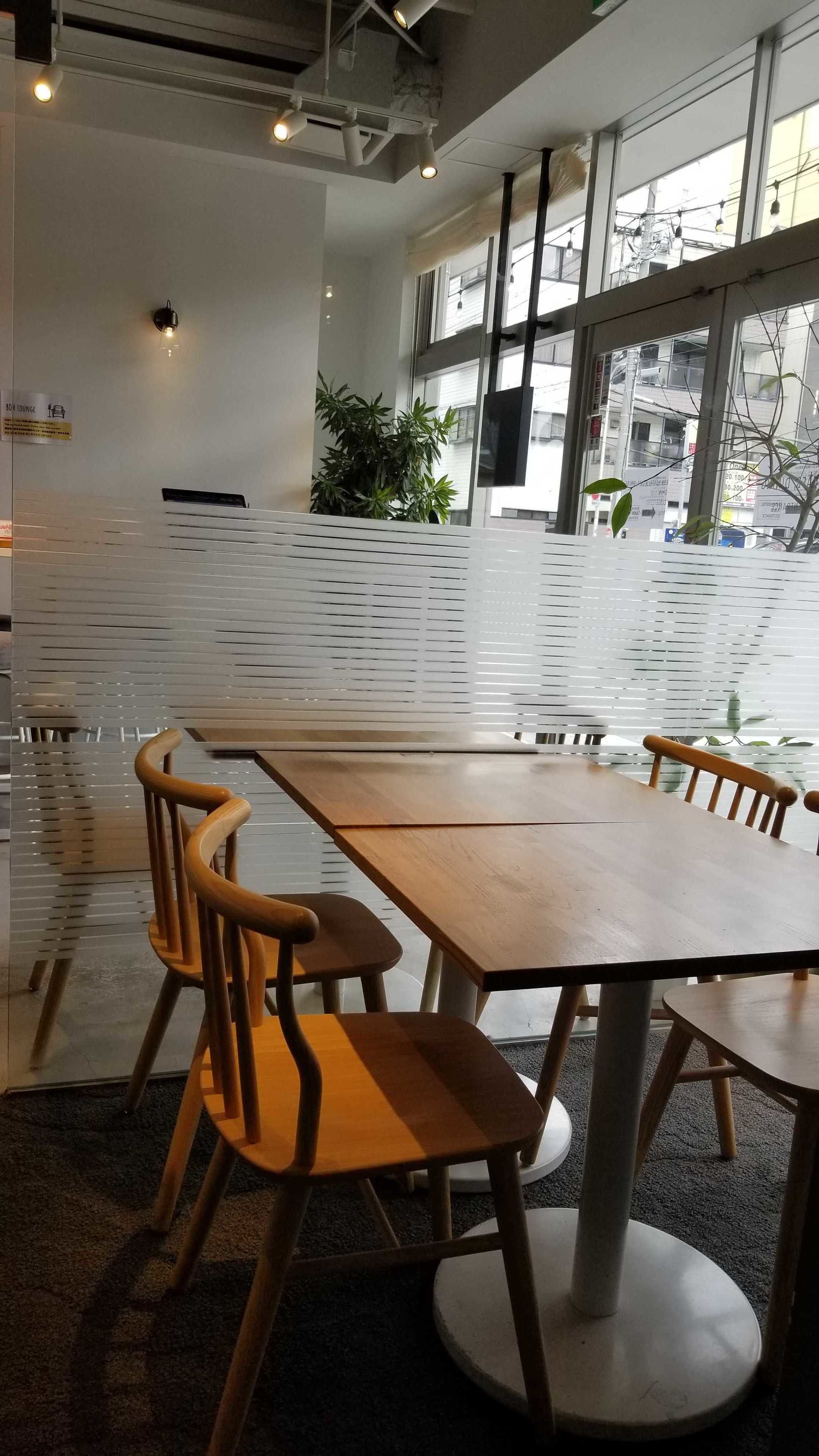Een moderne ruimte met een lange tafel en stoelen, grote ramen en een potplant.