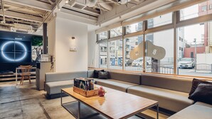 A modern interior with a seating area, a wooden table, and a large window offering a city view. - BON Hostel (Osaka)