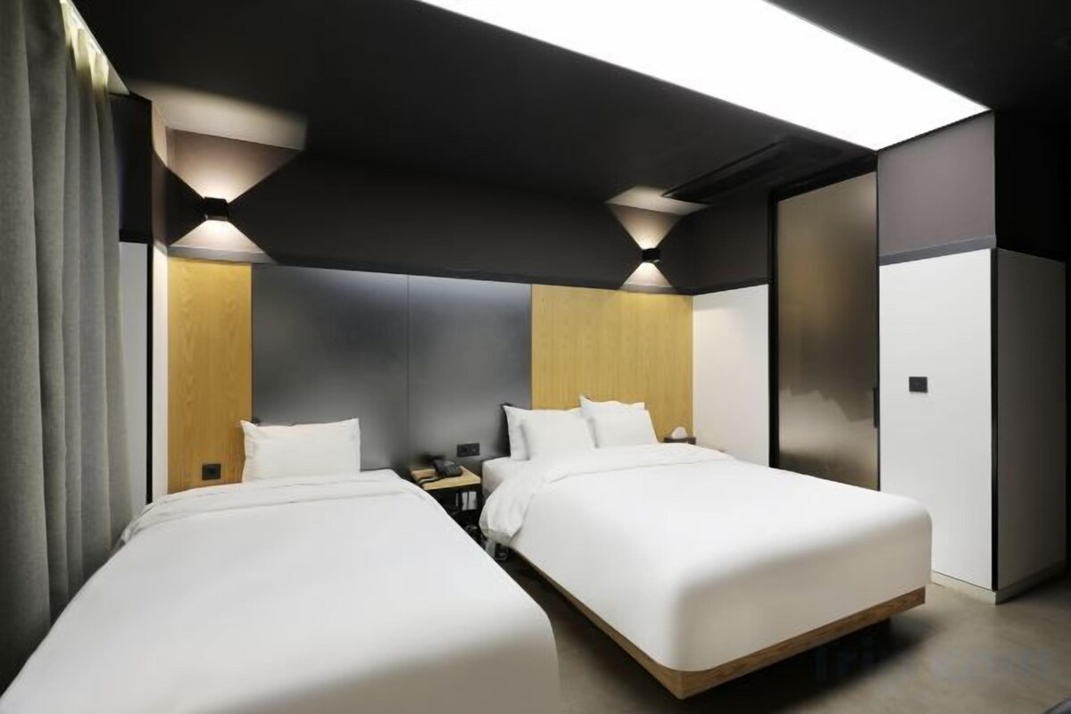 Ett modernt hotellrum med två sängar, ett sängbord och en inbyggd garderob.