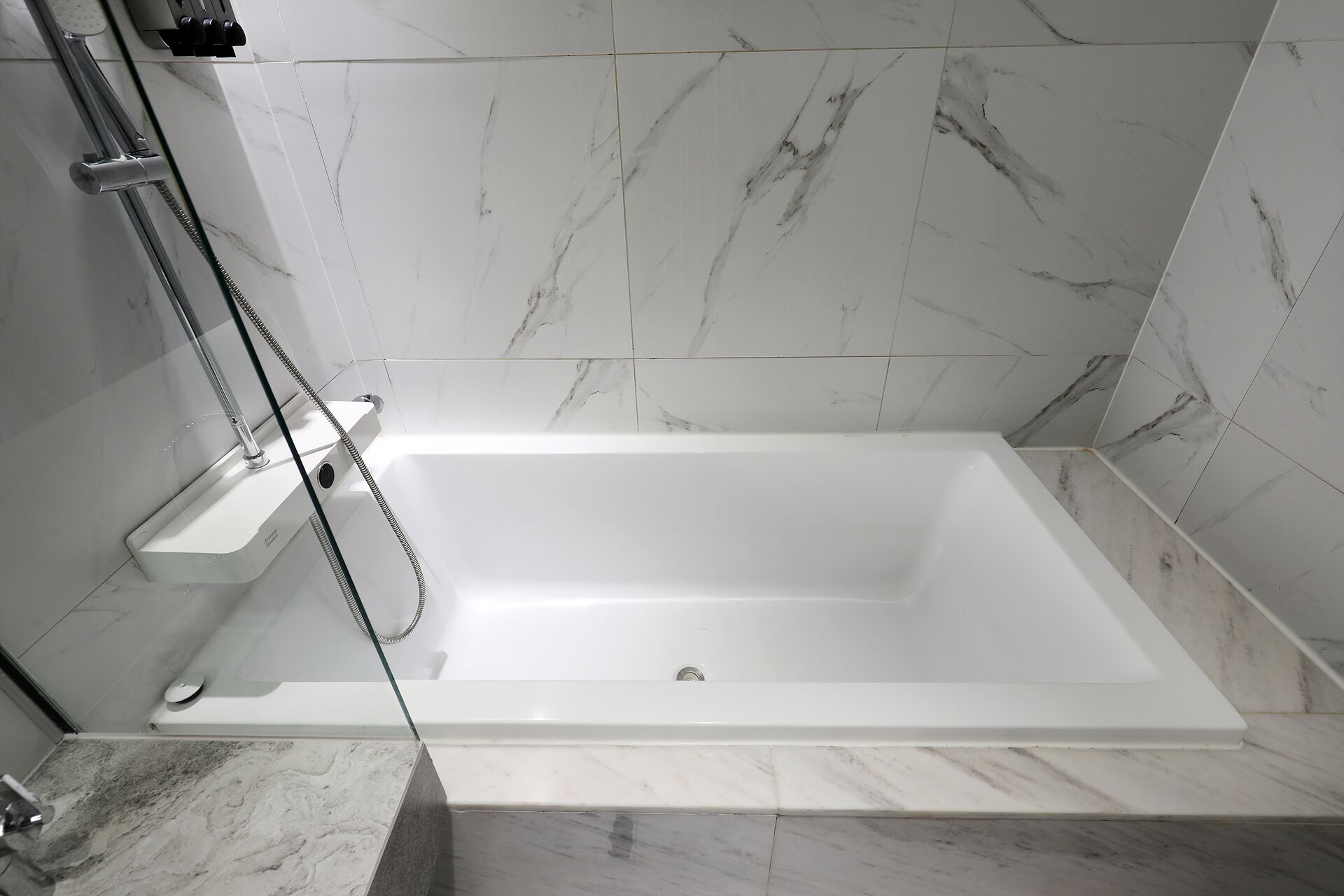 A modern bathroom with a white bathtub, a glass shower enclosure, and marble tiles.