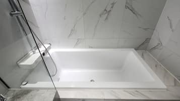 A modern bathroom with a white bathtub, a glass shower enclosure, and marble tiles.