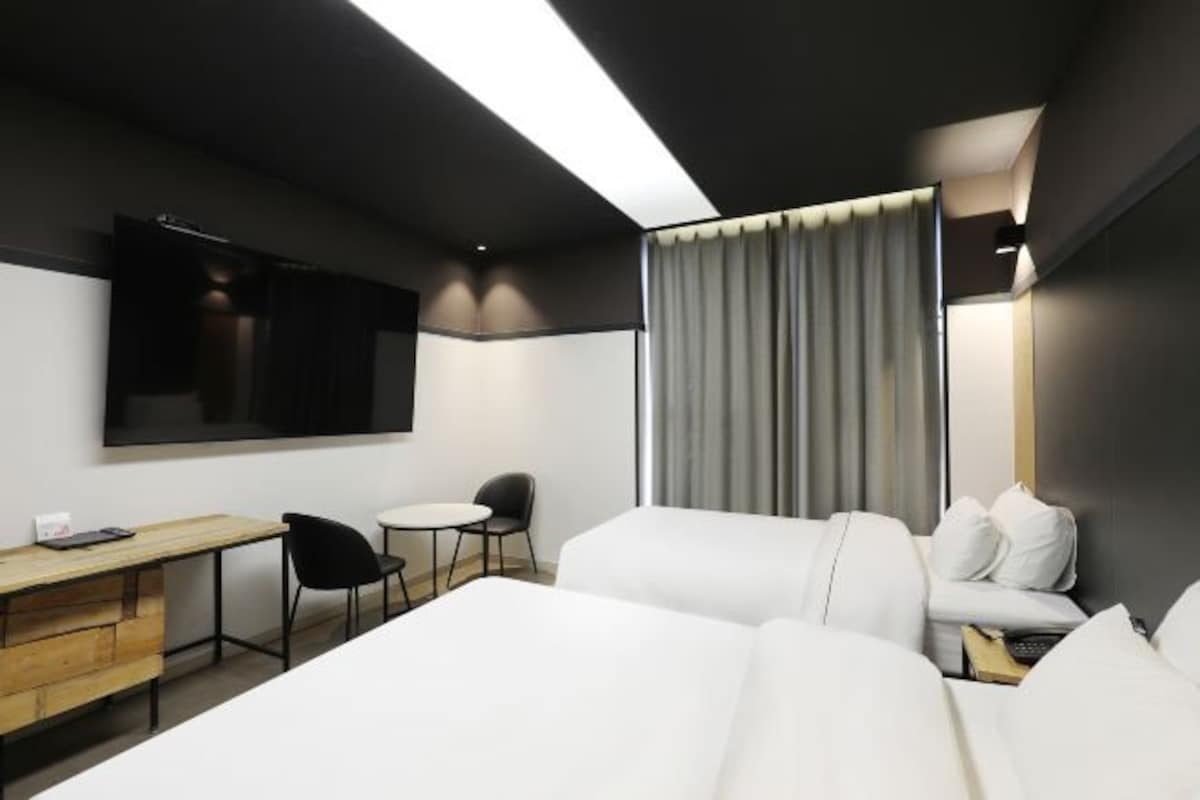 A modern hotel room with a large bed, a desk, a chair, a small table, and a TV.