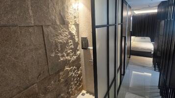 A modern bathroom with a stone wall, a glass partition, and a bed with a white mattress.