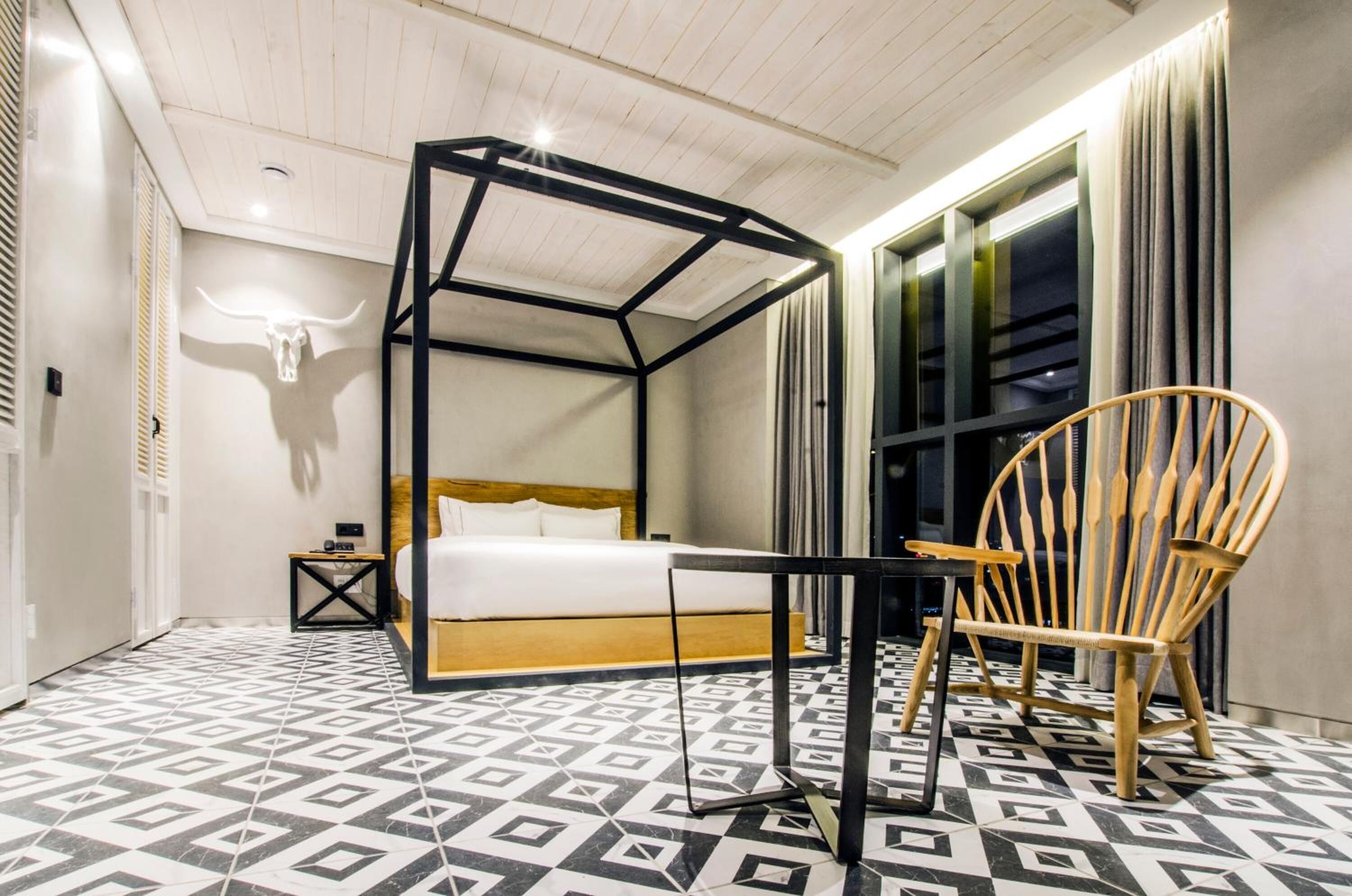 A modern bedroom with a four-poster bed, a wooden chair, and patterned flooring.
