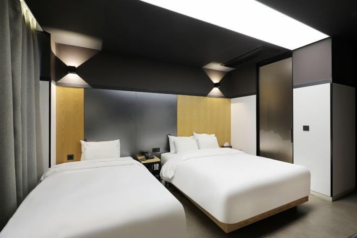 A modern hotel room with two beds, a wooden headboard, and a large window.
