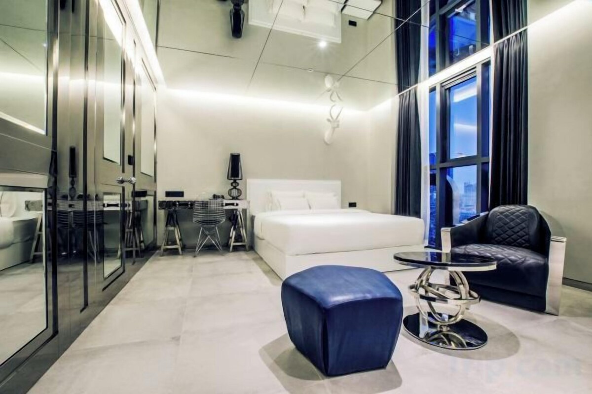 A modern hotel room with a bed, a desk, a chair, and a small table.