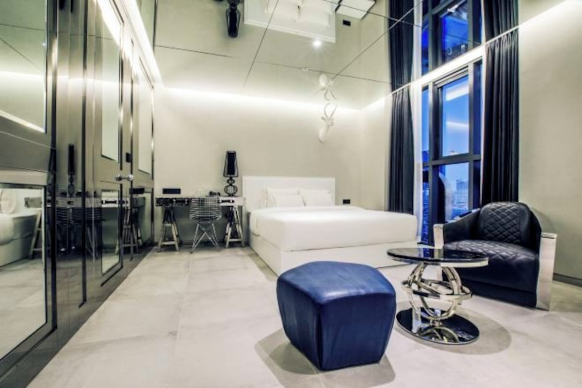 A modern hotel room with a large bed, a desk, a chair, and a small round table.