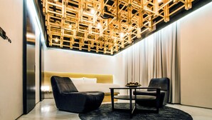 Una sala moderna con techo de madera geométrico, un sofá de cuero negro, una mesita y un sofá blanco.
