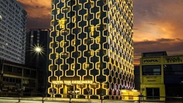 Un hotel alto con una fachada geométrica distintiva y ventanas iluminadas al caer la noche.