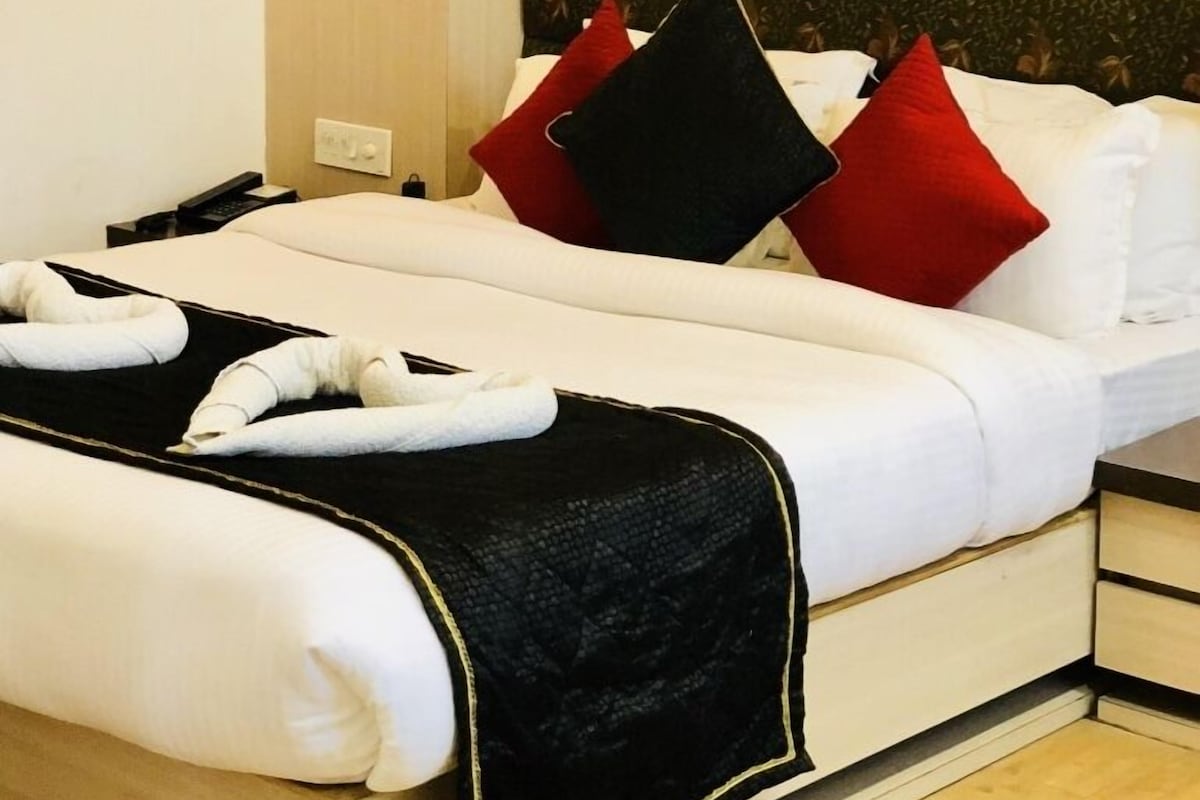 A hotel room with a bed, pillows, a blanket, and a headboard with a leaf pattern.