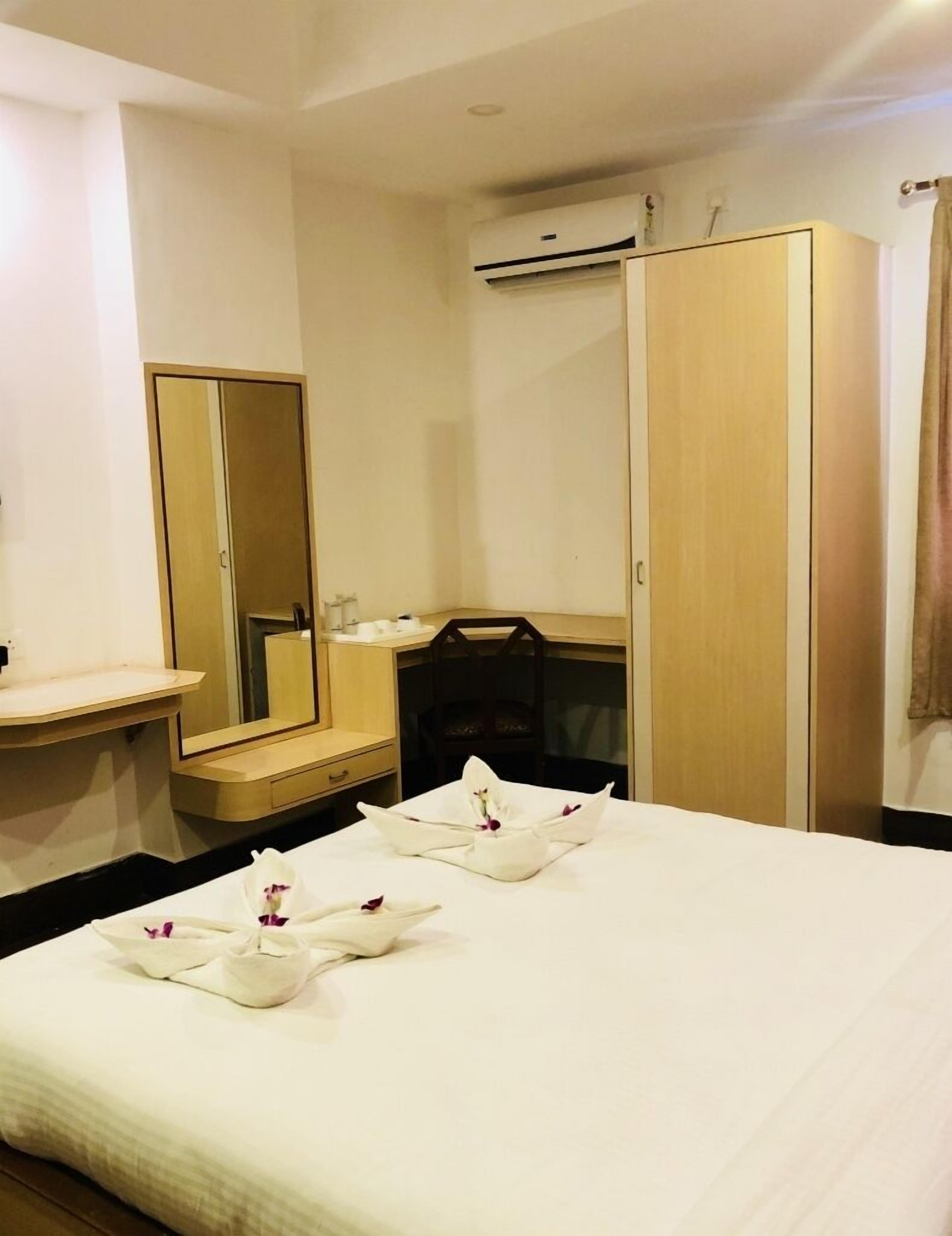 A hotel room with a bed, a bedside table, a mirror, a wardrobe, and an air conditioning unit.