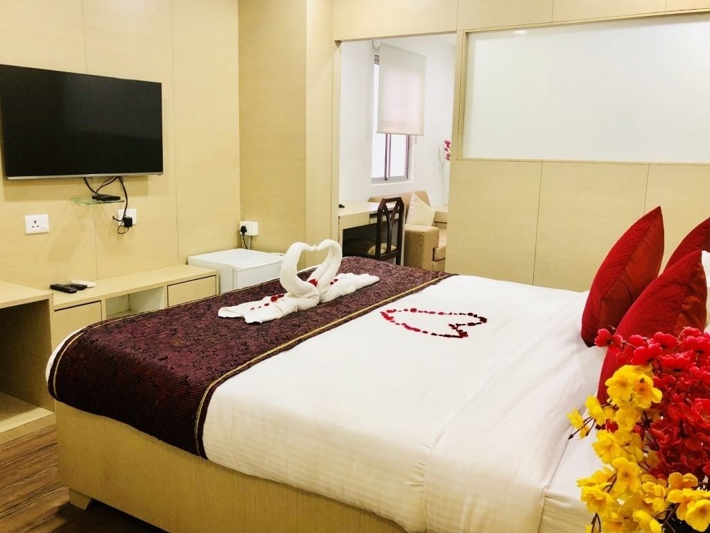 A hotel room with a bed, a TV mounted on the wall, a desk, and a chair.