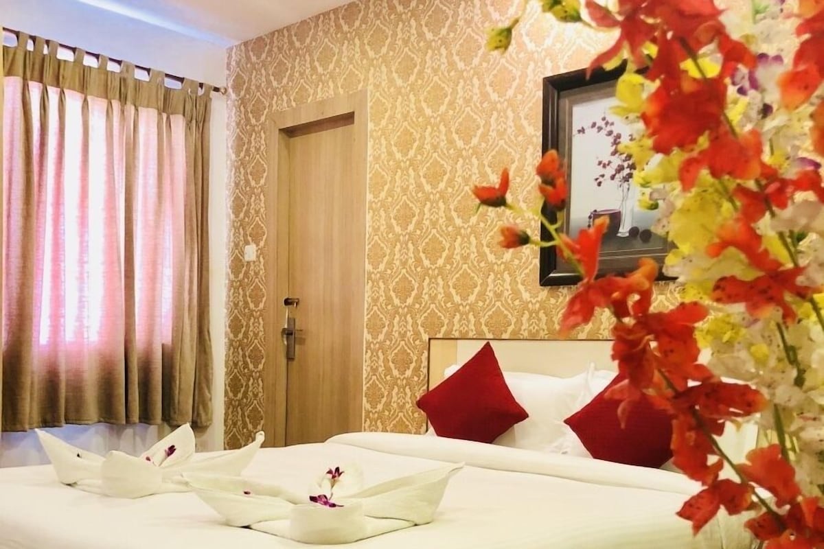 A neatly made bed with white linens and red pillows, a wooden door, and patterned wallpaper.