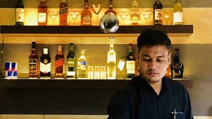 Zona de bar con estantes llenos de botellas de licor y una persona sosteniendo una copa de martini.