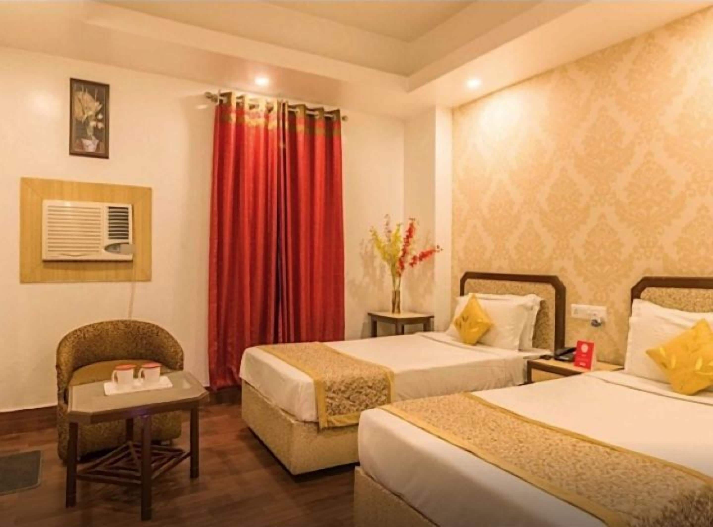 Une chambre d’hôtel avec deux lits, une petite table avec une chaise, un vase avec des fleurs et un climatiseur fixé au mur.