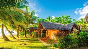 A tropical resort with thatched-roof cottages, lush greenery, and a clear view of the ocean.
