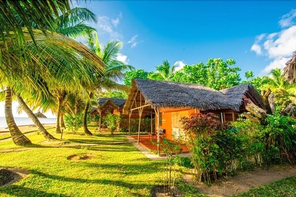 Un resort tropical con cabañas de techo de paja, exuberante vegetación y una vista despejada del océano.