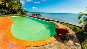 A swimming pool with a curved edge, surrounded by a stone deck and a wooden walkway.