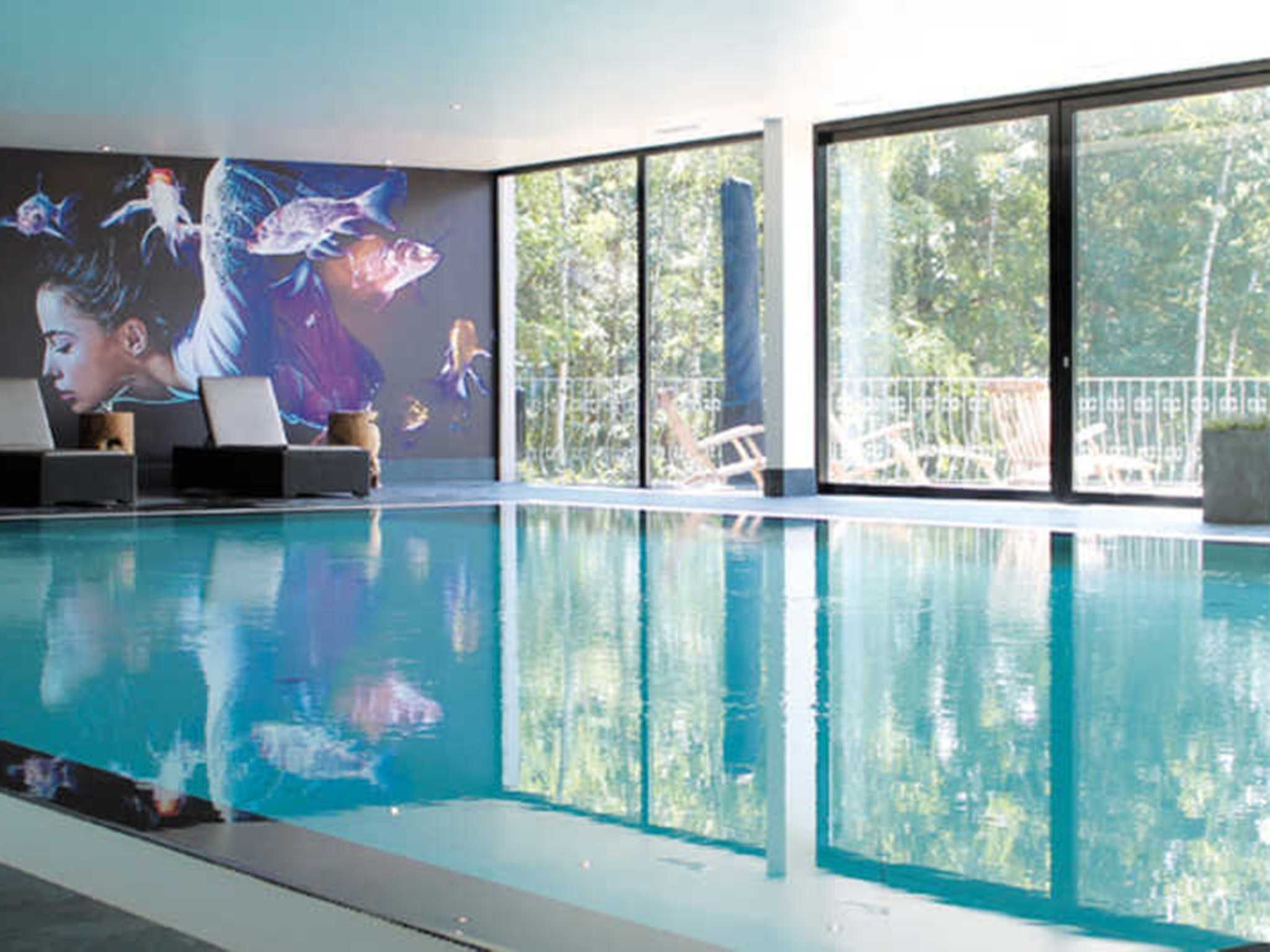 An indoor swimming pool with clear water, a mural with aquatic themes, and large windows offering a view of the outdoors.