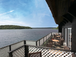 A deck with outdoor seating overlooking a lake, a thatched roof structure, and a forested island in the distance.