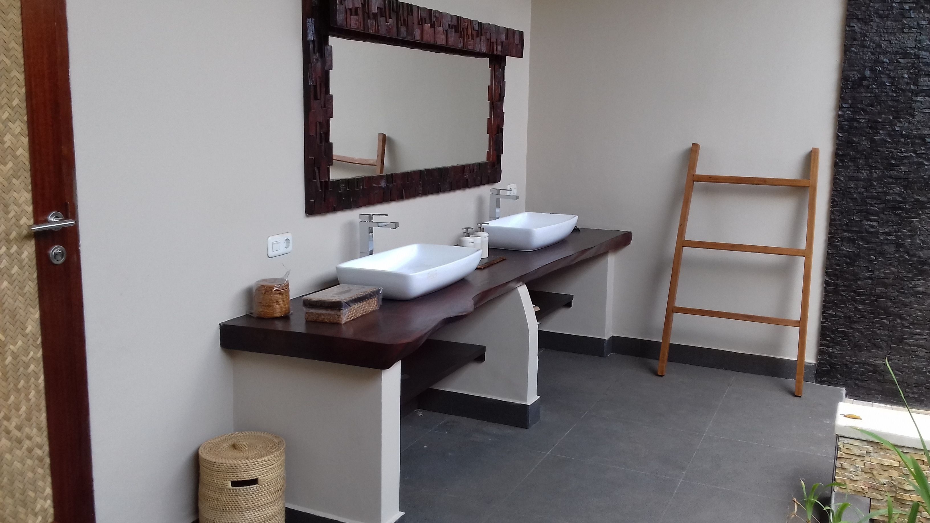 A bathroom with two white sinks, a wooden ladder, and a woven basket.