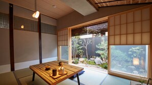 Een traditionele Japanse kamer met tatami vloeren, een lage tafel met theeaangezet en uitzicht op een tuin door shoji schermen.
