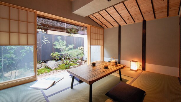 Een traditionele Japanse kamer met tatami vloeren, een lage houten tafel, een lantaarn en uitzicht op een tuin door een glijdende deur.