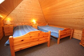 Um quarto de sótão com painéis de madeira, duas camas de madeira, mesas de cabeceira com luminárias e piso coberto por carpete.