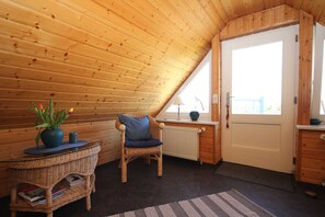 A cozy room with a sloped ceiling, a wicker chair, a small table with a vase, a radiator, and a door with a view. - Apartment Hinz - Apartment Hinz (Wustrow)