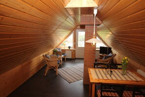 A cozy attic room with wooden walls, a dining table, chairs, a TV, and a window. - Apartment Hinz - Apartment Hinz (Wustrow)