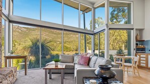 A spacious living area with a large window, a sofa, a coffee table, and a kitchen area. - Bushland (Halls Gap)